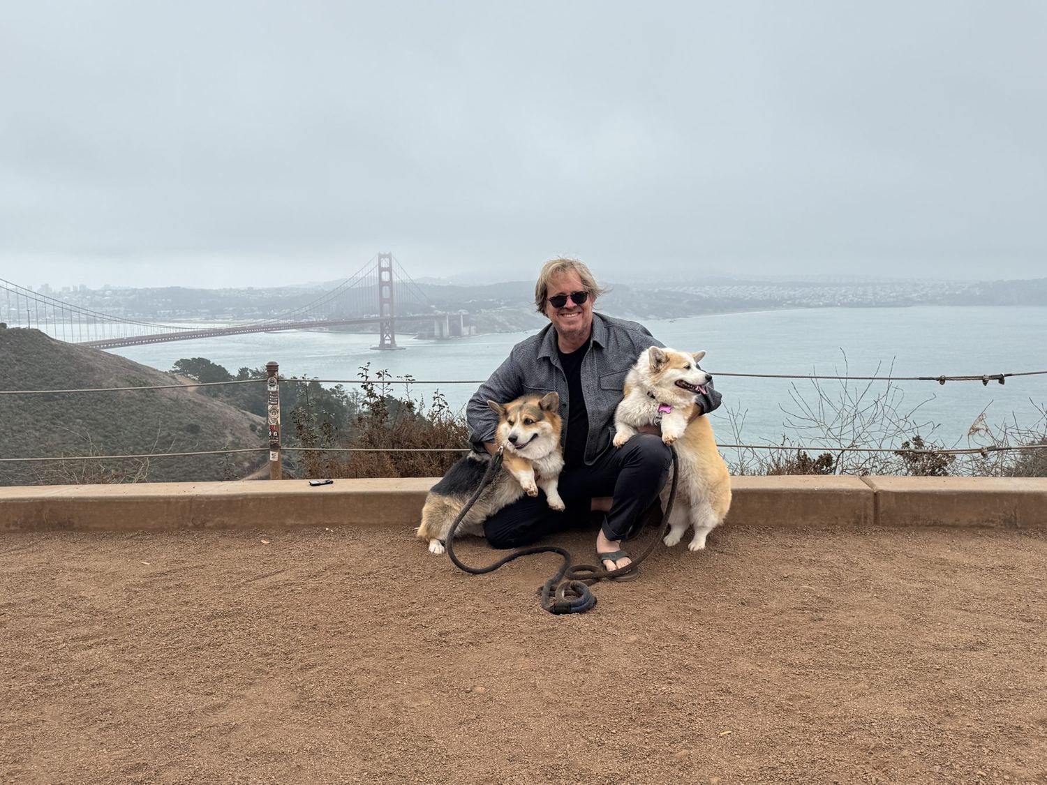 Matt crouching with Orbit and Astra at an overlook, the Golden Gate Bridge in fog behind them