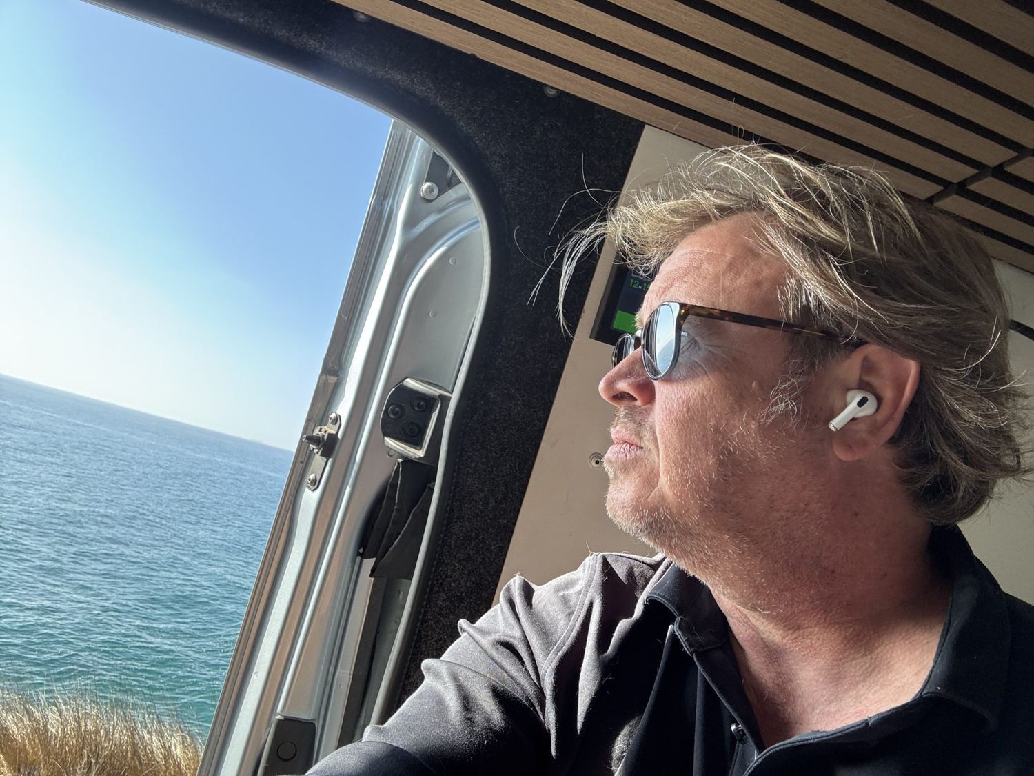 Matt in profile at the van's open door, sunglasses on, looking out at the ocean